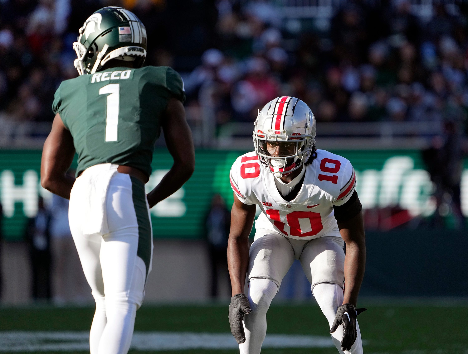 Caption: Oct 8, 2022; East Lansing, Michigan, USA; Ohio State Buckeyes cornerback Denzel Burke (10) goes up against Michigan State Spartans wide receiver Jayden Reed (1) in the third quarter of the NCAA Division I football game between the Ohio State Buckeyes and Michigan State Spartans at Spartan Stadium.