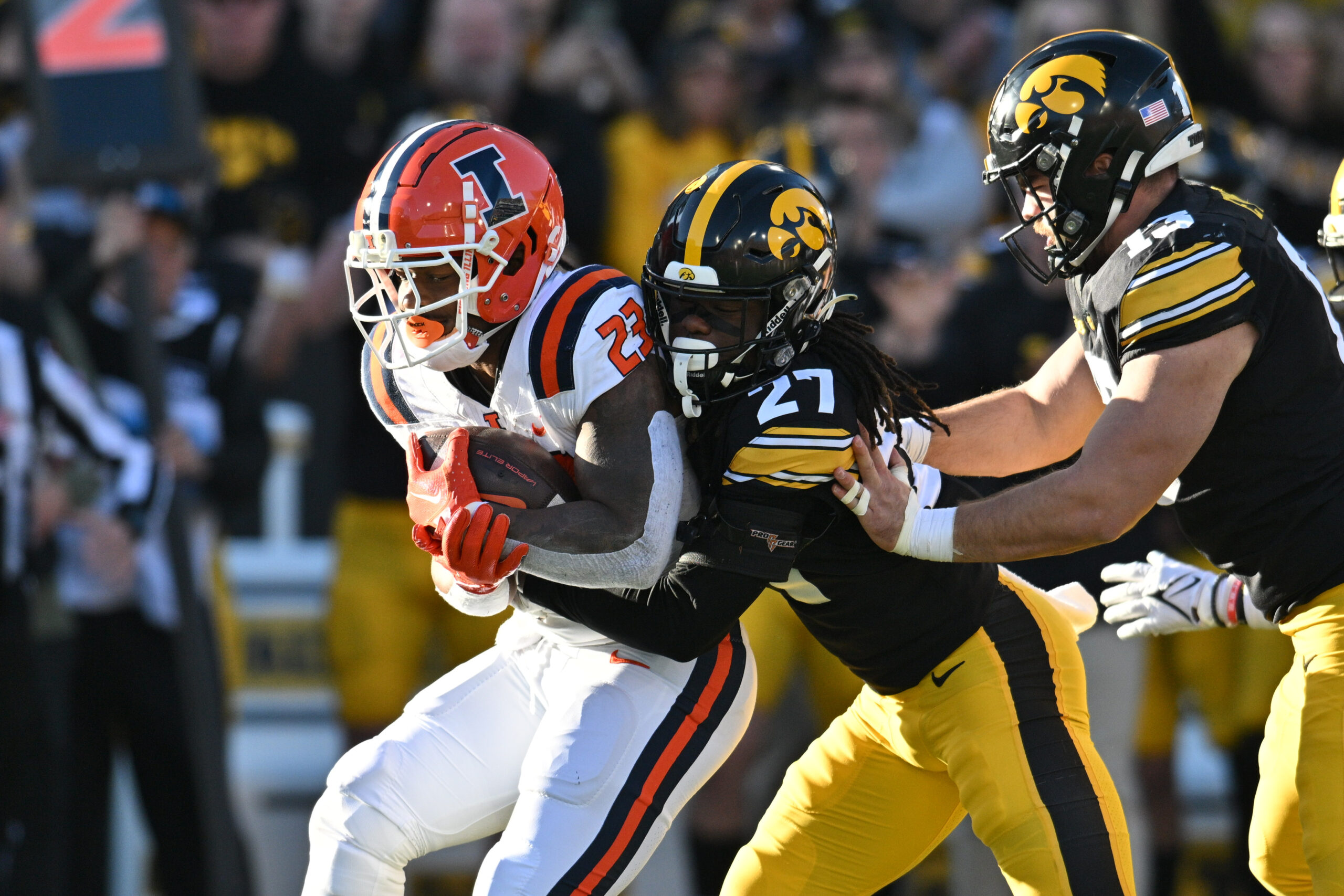 Nov 18, 2023; Iowa City, Iowa, USA; Illinois Fighting Illini running back Reggie Love III (23) is stopped by Iowa Hawkeyes defensive back Jermari Harris (27) and defensive end Joe Evans (13) during the first quarter at Kinnick Stadium.