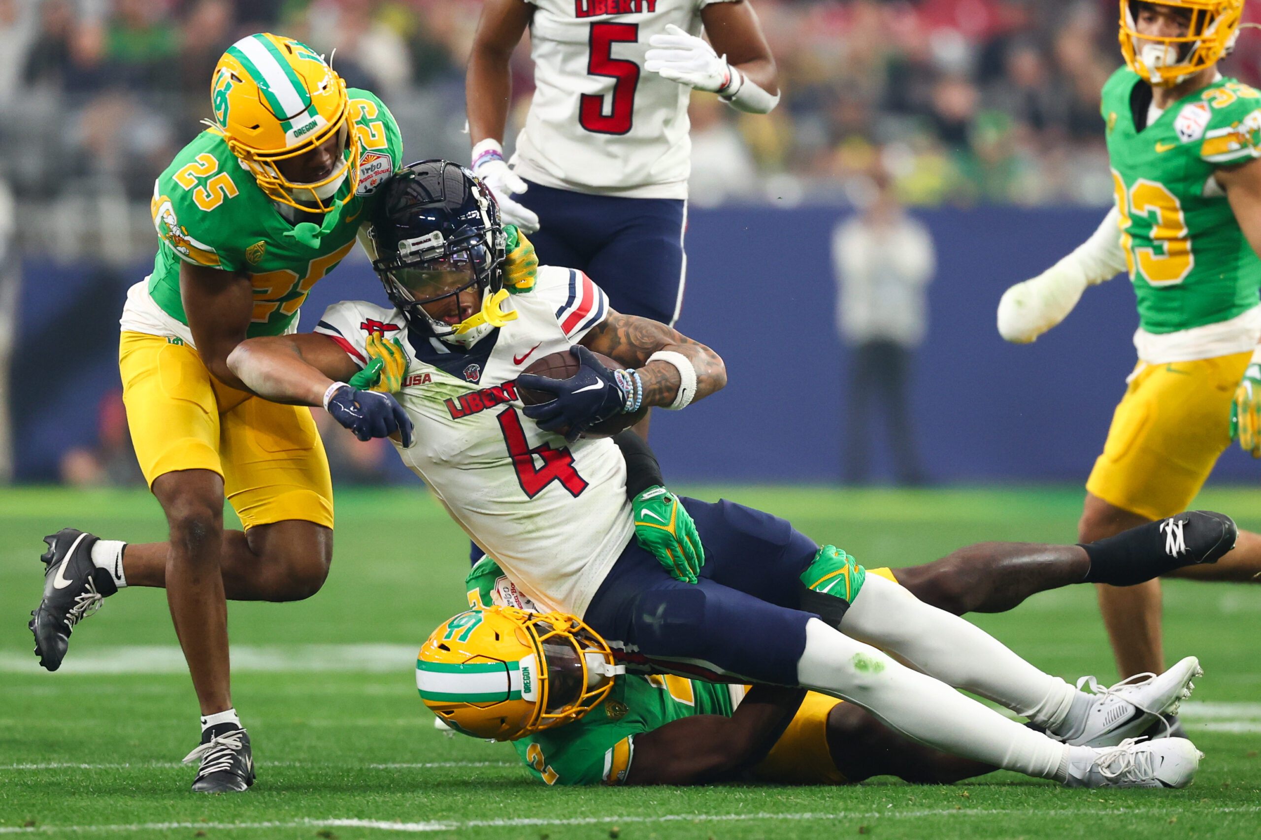 Jan 1, 2024; Glendale, AZ, USA; Liberty Flames wide receiver CJ Daniels (4) is tackled by Oregon Ducks defensive back Nikko Reed (25) and linebacker Jeffrey Bassa (2) during the first quarter of the 2024 Fiesta Bowl at State Farm Stadium. Mandatory Credit: Mark J. Rebilas-USA TODAY Sports