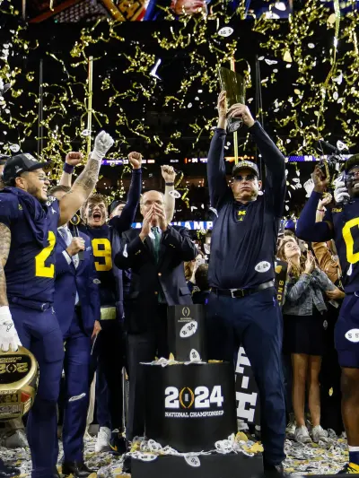 Michigan head coach Jim Harbaugh lifts up the trophy as players and coaches celebrate after their 34-13 win over Washington to win the national championship at NRG Stadium in Houston on Monday